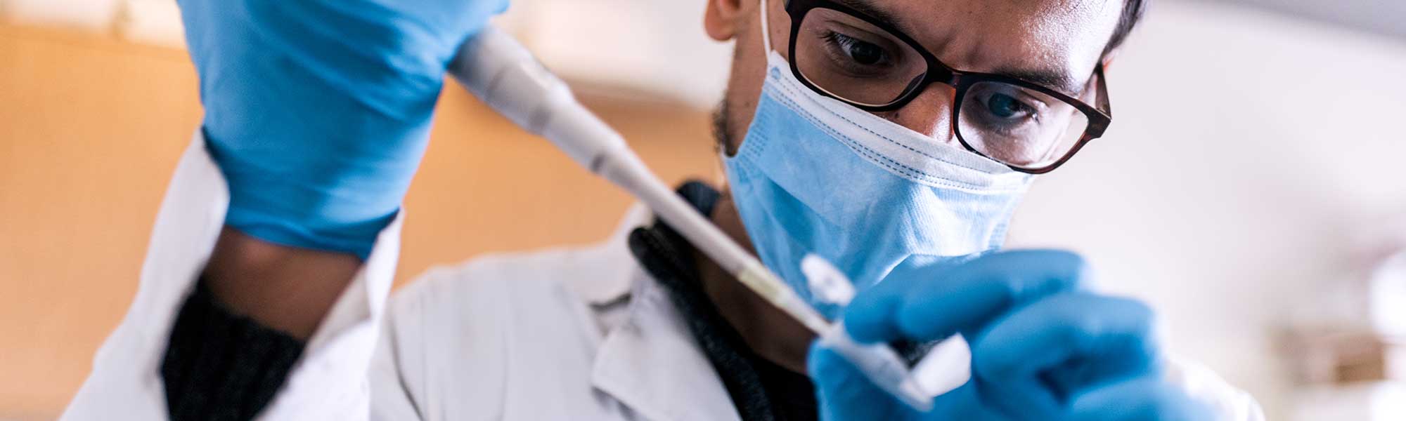 Science researcher wearing face mask filling test tubes in his laboratory.